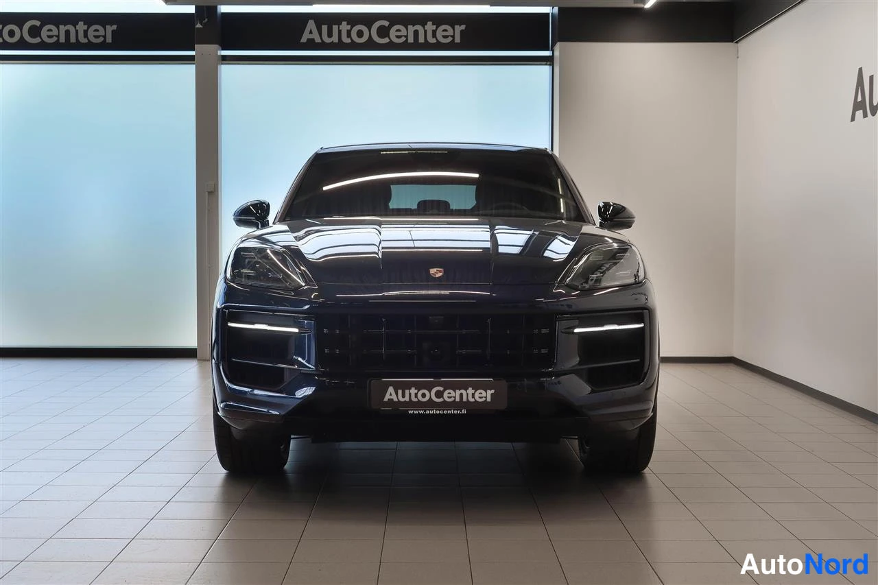 Edestä: Edestä kuvattu tummansininen auto showroomissa; etusäleikkö, ajovalot ja etupuskuri näkyvät suoraan edestä, kyltillä AutoCenter-tekstit.
