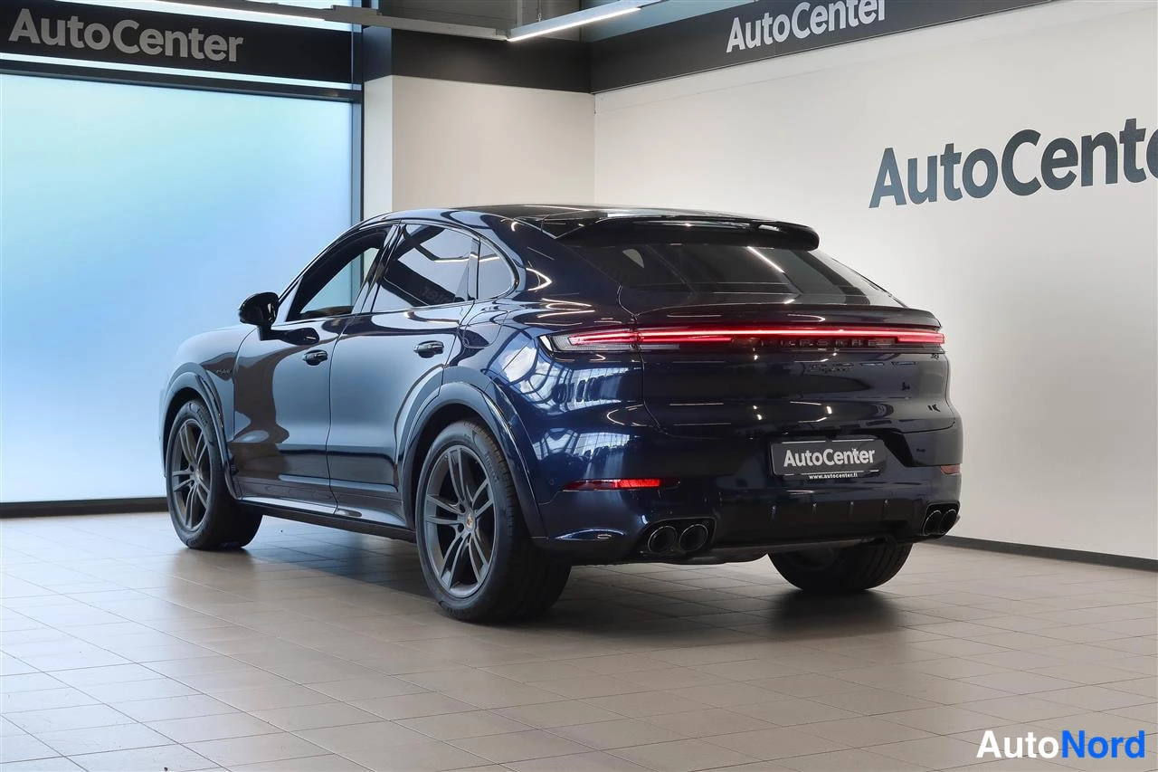 Takaviisto: Porsche Cayennen takakulma hallissa: punainen takavalokiista, kaksoispakoputket ja AutoCenter-kyltti.