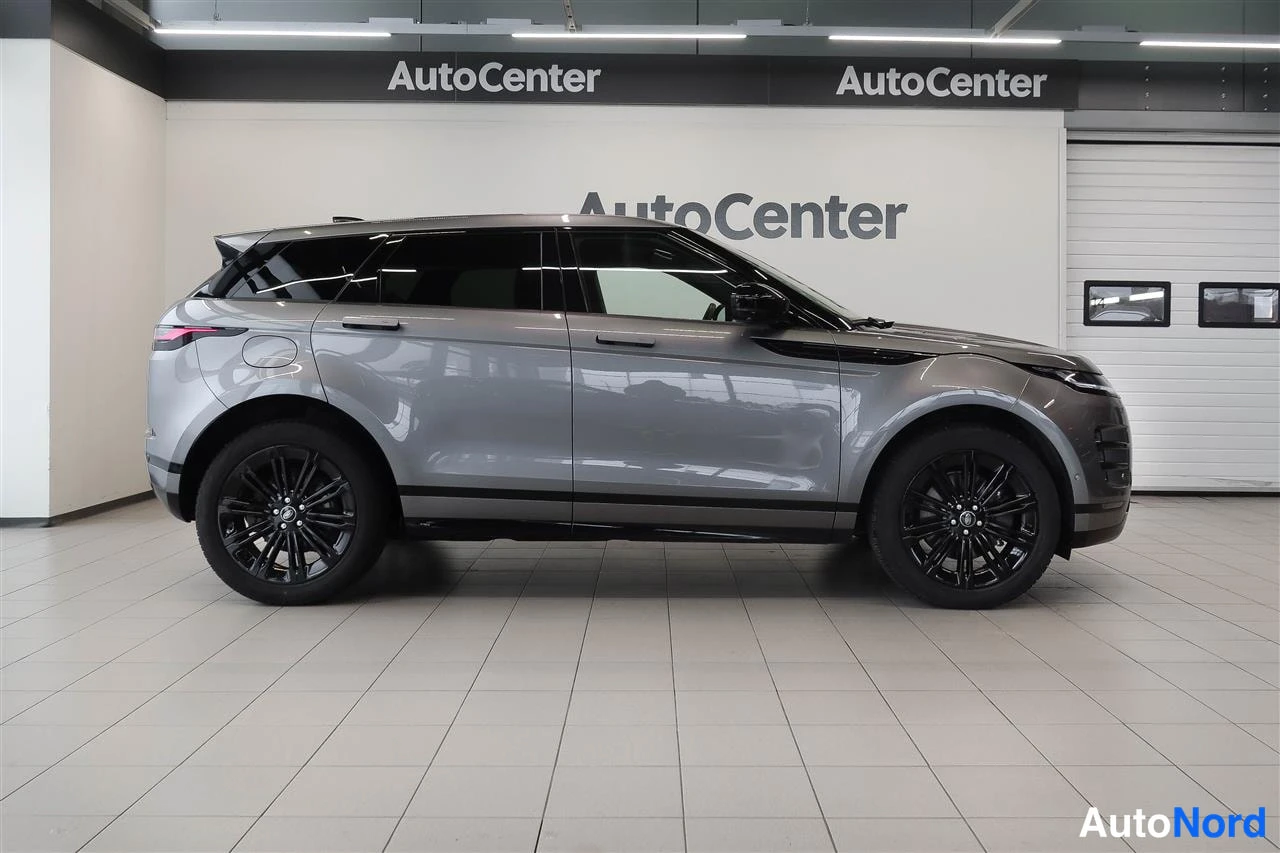 Sivulta: Hopeanharmaa Range Rover Evoque sivuprofiili oikealta, mustat vanteet, AutoCenter-näyttö taustalla.