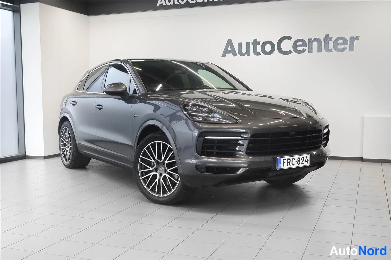 Etuviisto, nokka oikealle: Harmaa Porsche Cayenne Coupé kulmasta kuvattuna showroomissa, rekisterikilpi.