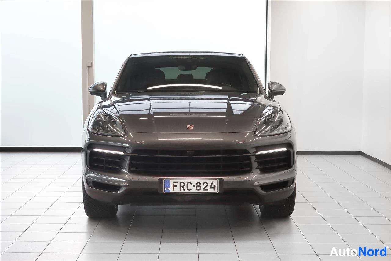 Edestä: Harmaa Porsche Cayenne Coupé suoraan edestä kuvattuna showroomissa, rekisterikilpi.