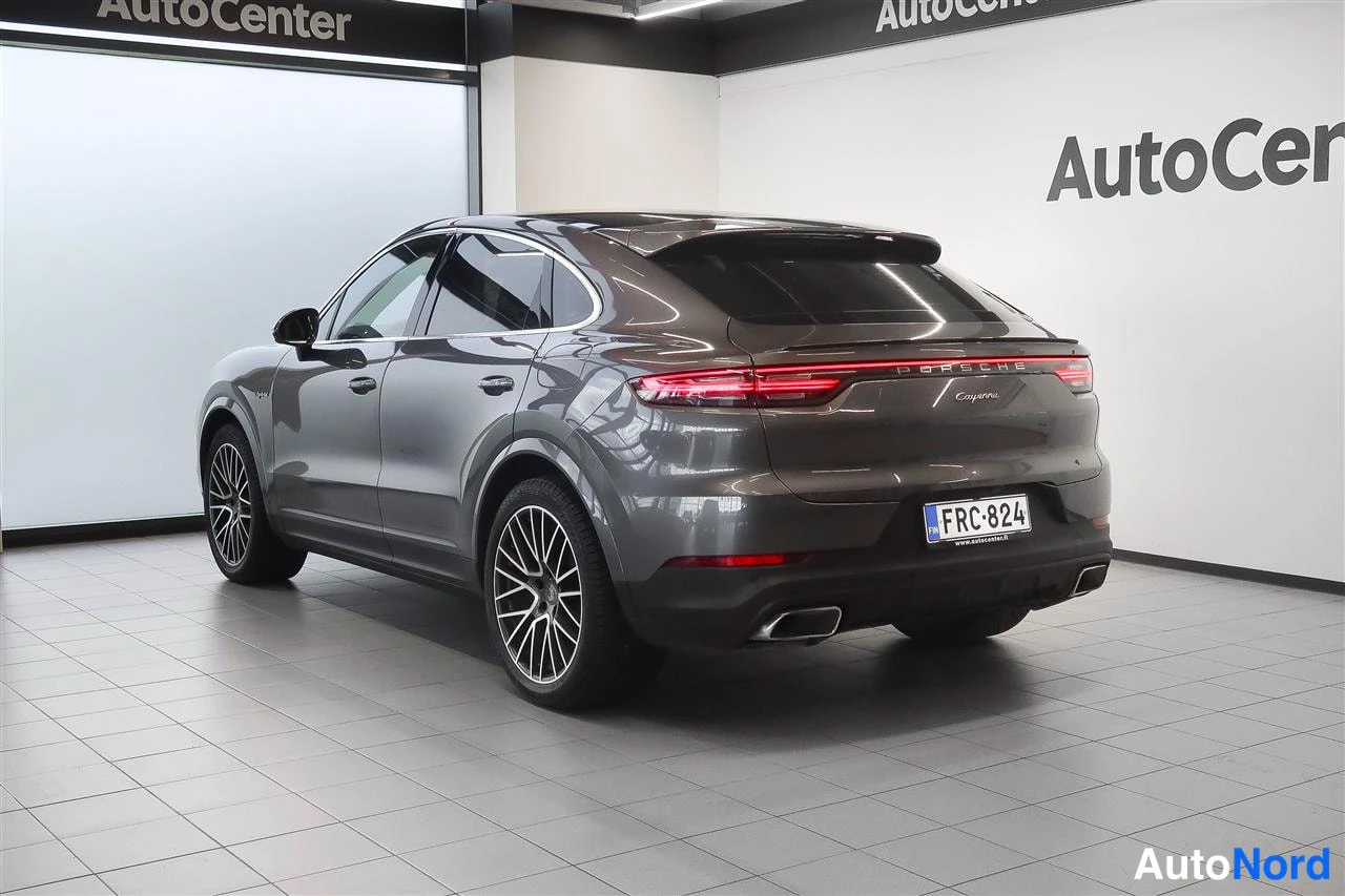 Takaviisto: Takanurkkakuva autosta sisätiloissa; tummanharmaa coupé-SUV, takavalojauo, PORSCHE- ja Cayenne-teksti takaluukussa, rekisterikilpi, kaksi pakoputkea.