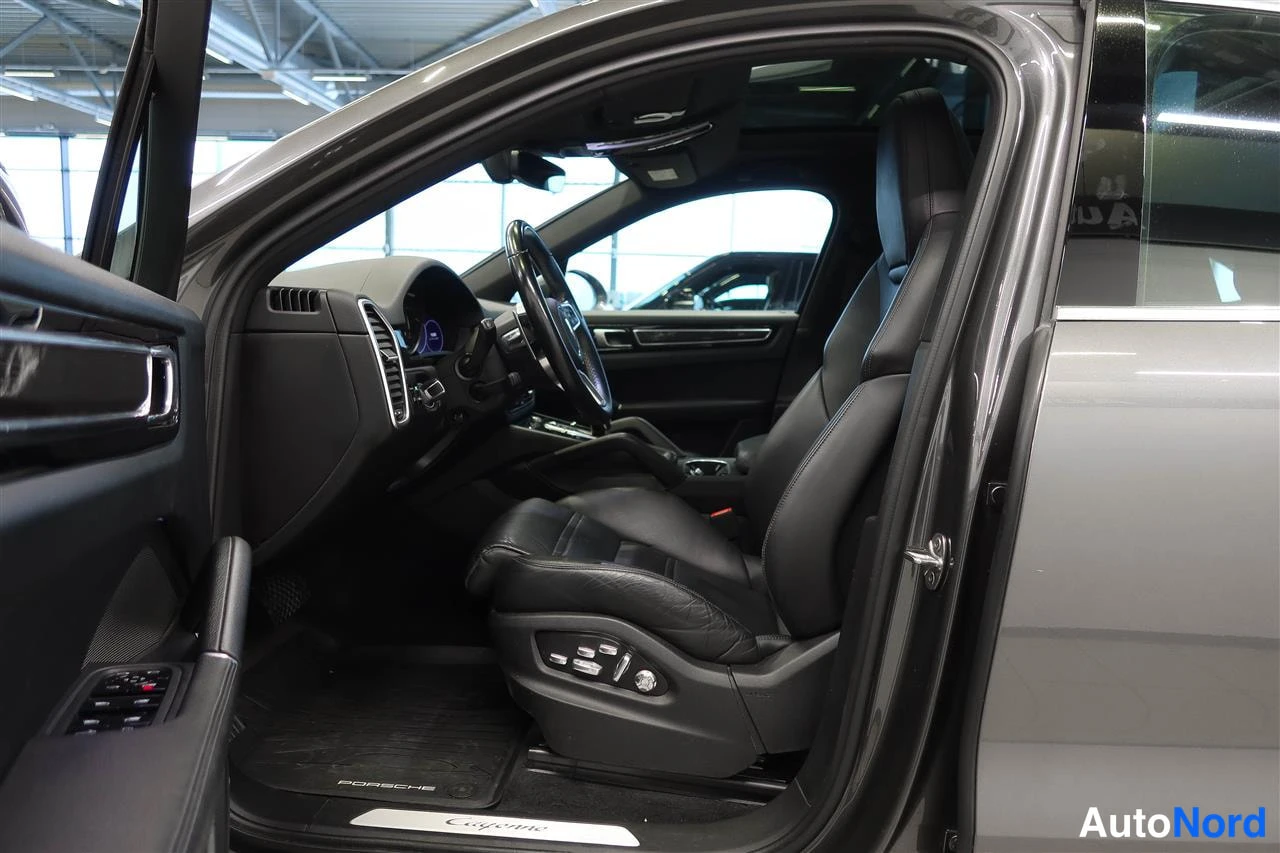 Muu: Avattu kuljettajan ovi: Porsche Cayennen tumma sisätilo, joissa musta nahkapenkki, roolitussäädöt ja PORSCHE-matto.