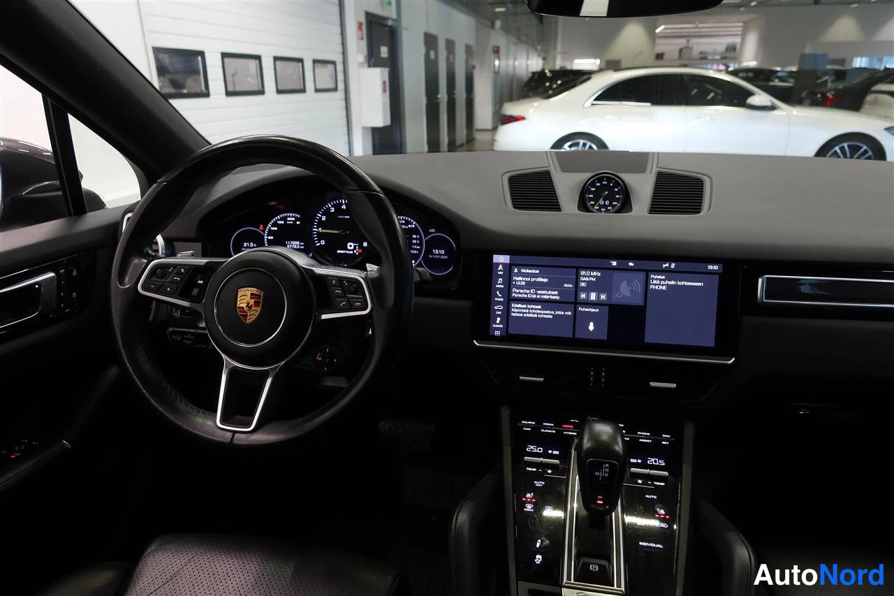 Muu: Kuljettajan näkymä Porsche Cayennen ohjaamoon: Porsche-tunnuksellinen ohjauspyörä, digitaalinenmittaristo, keskinäyttö ja kosketusnäytöllä toimiva viihdejärjest