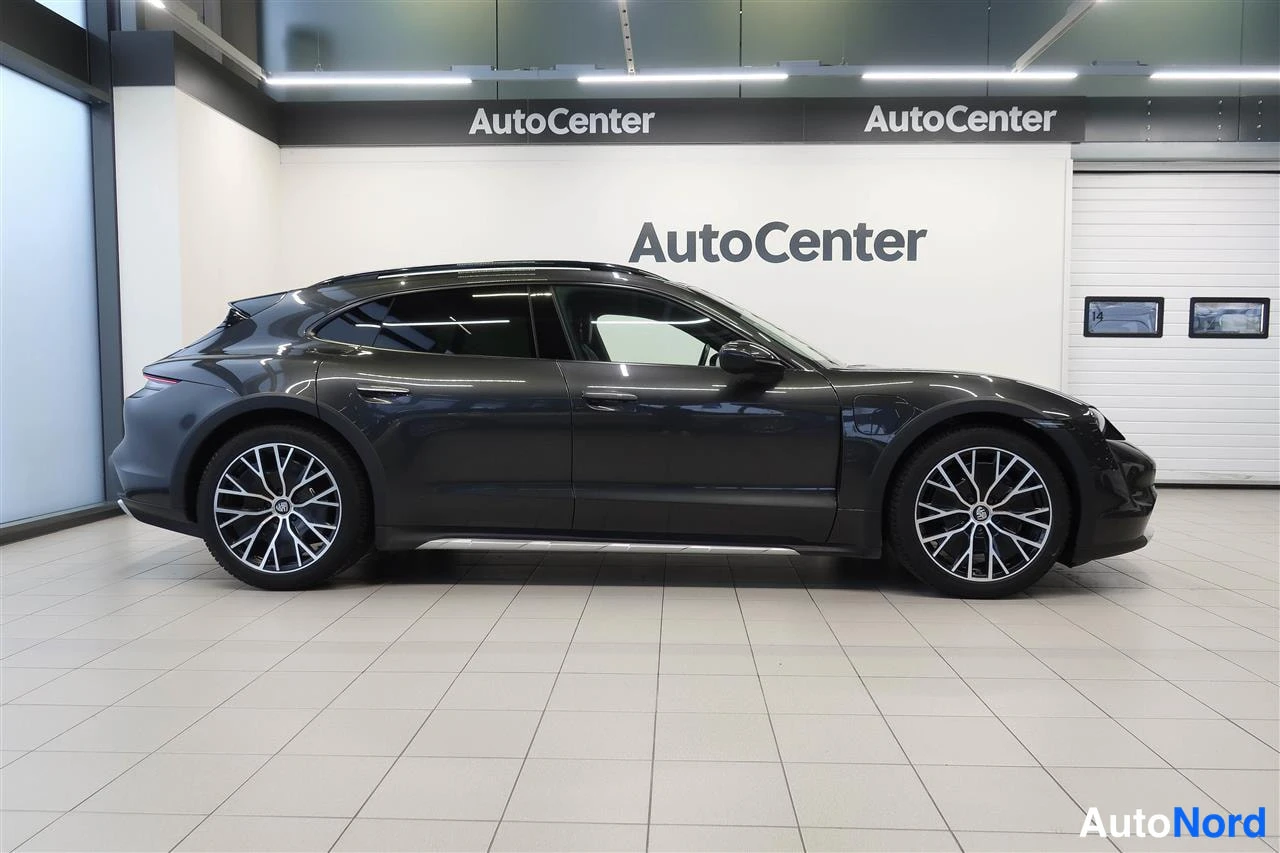 Sivulta: Sivulta kuvattu tummanharmaa Porsche Taycan Cross Turismo autosalissa.