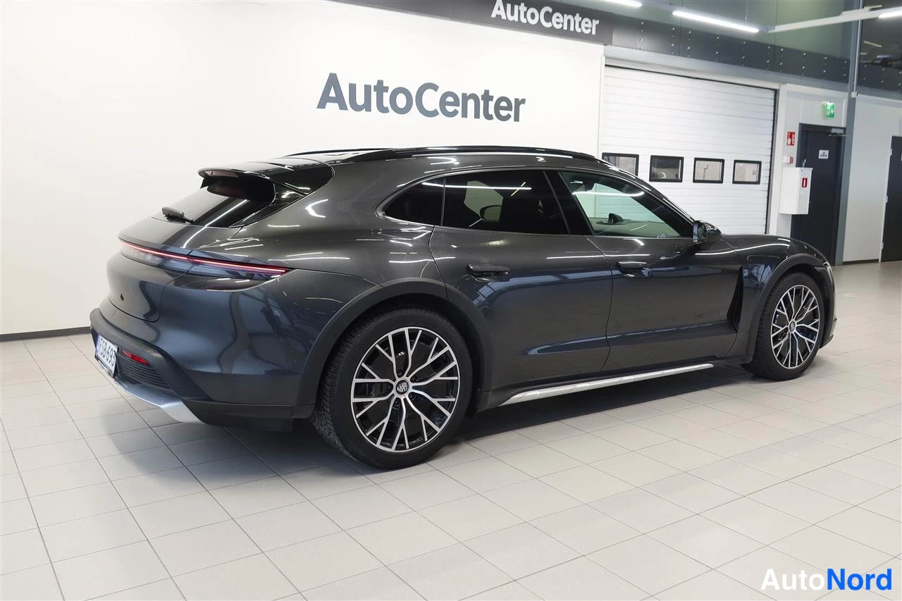 Takaviisto: Tummanharmaa Porsche Taycan Cross Turismo takakulma-autosalissa, takavalo raitana.