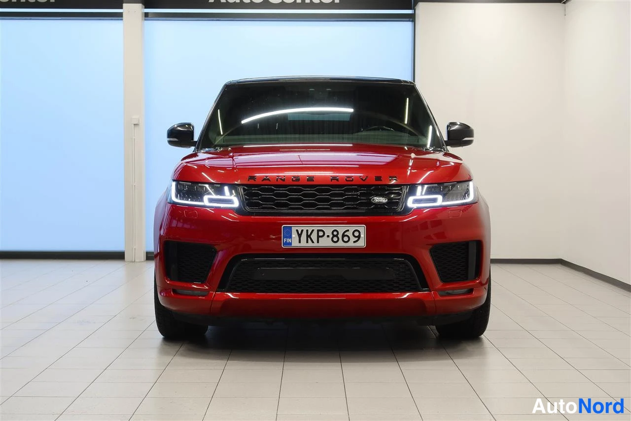 Edestä: Punaisen Land Rover Range Rover Sport -maasturin edestäpäin otettu kuva, LED-ajovalot päällä.