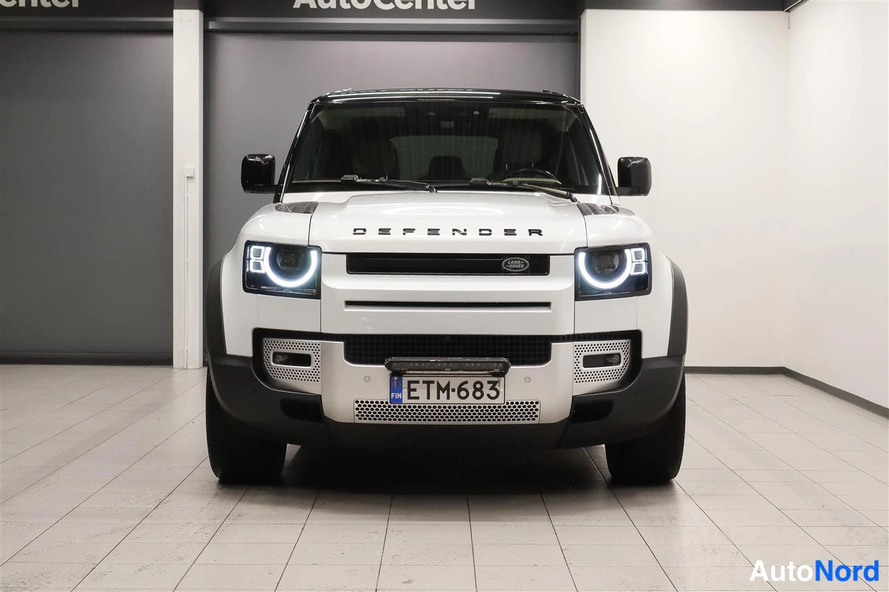 Edestä: Land Rover Defenderin etupää suoraan edestä, valkoinen kori, DEFENDER-teksti konepellissä, rekisteritunnus.