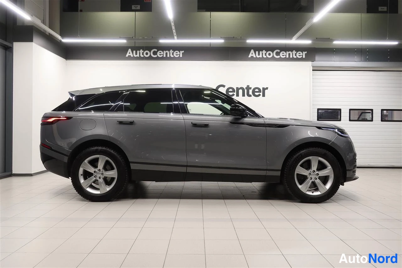 Etuviisto, nokka oikealle: Land Rover Range Rover Velar, harmaa, sivukulmaisträjätä sisätiloissa, nokka oikealla.