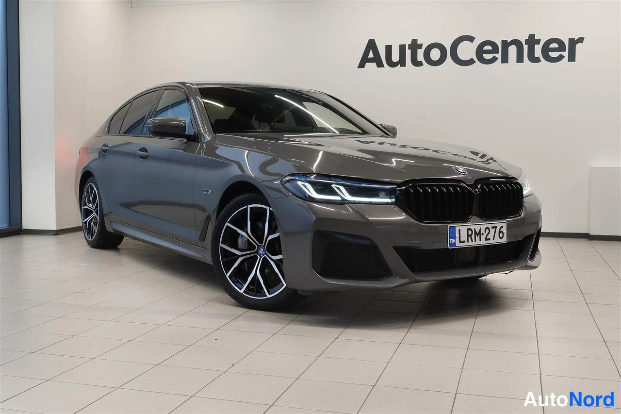 Etuviisto, nokka oikealle: BMW 5-sarjan sedan etuviistosta oikealta, harmaankarma kolovi vaalealla lattialla, rekisteritunnus.
