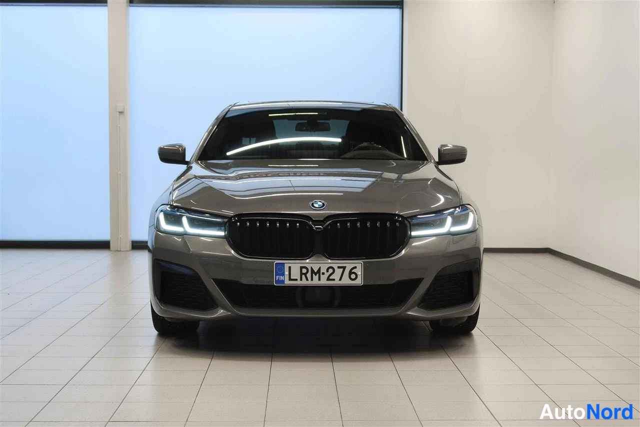 Edestä: BMW 5-sarjan sedan suoraan edestäpäin, harmaankarma, musta etusuoja, rekisteritunnus.