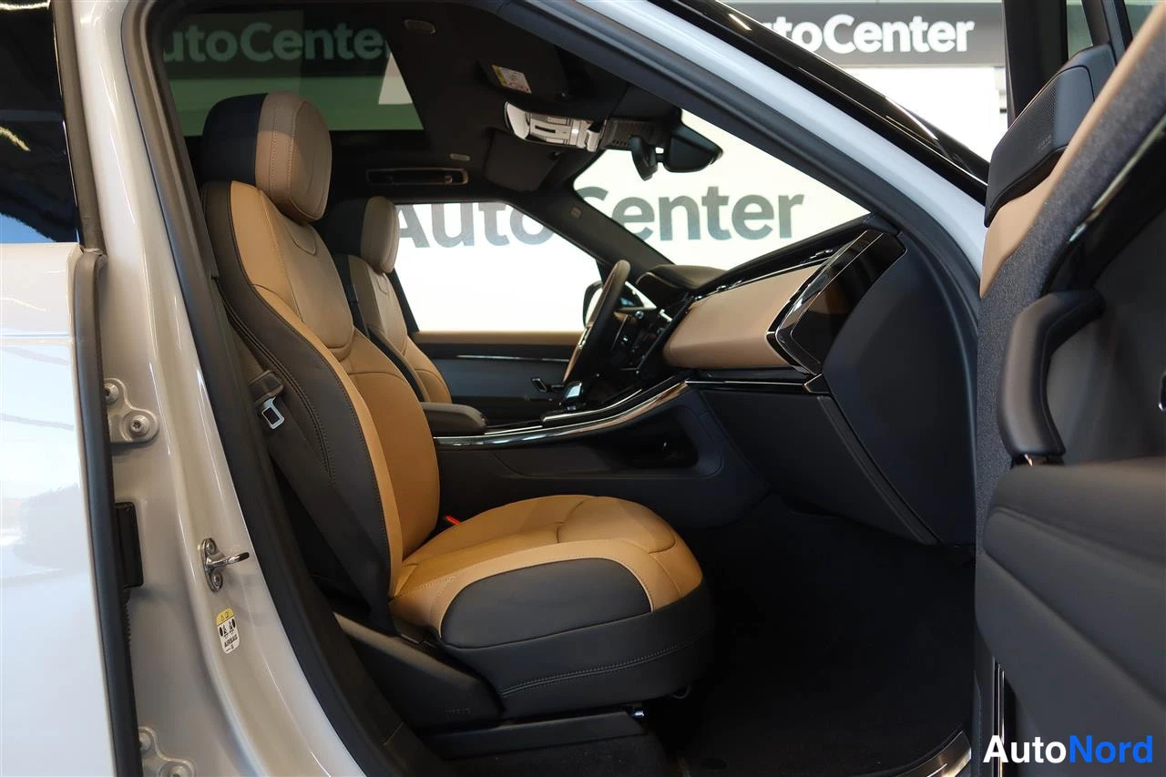 Sivulta: Avautunut kuljettajan ovi paljastaa auton etuistuimet, jotka ovat kaksiväriset beige-mustat nahat, tumma kojelauta ja lasikatto; taustalla AutoCenter-kyltti.