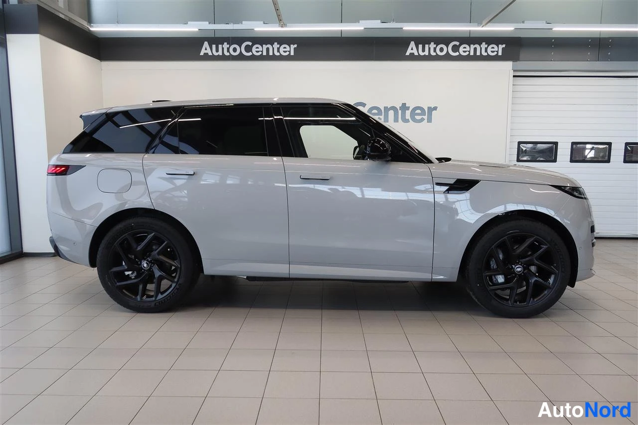Takaviisto: Hopeanharmaa Range Rover Sport takaolmasosakuvassa autoliikkeen hallissa, takavalo näkyvissä.