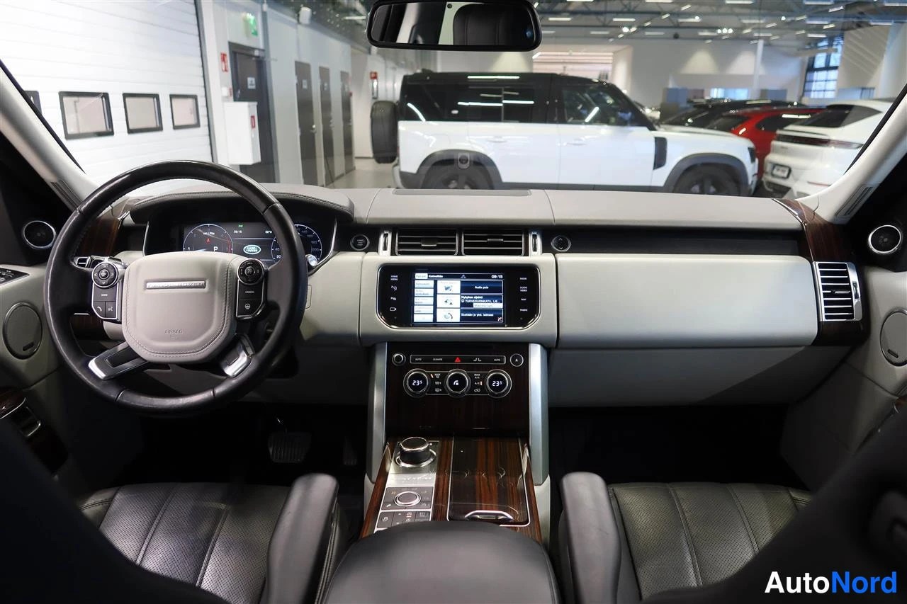 Edestä: Land Rover Range Roverin kojelauta ja ohjauspyörä edestäpäin; näkyy keskikonsolin näyttö ja vaihteiston valitsin.