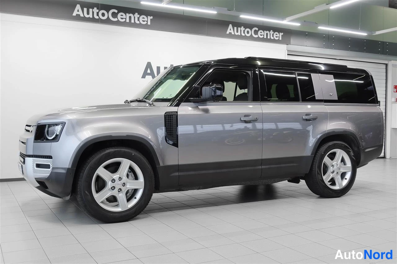Etuviisto, nokka vasemmalle: Land Rover Defender 130:n etuosakulmakuva sisätiloissa, keula vasemmalla, harmaa kori, musta katto ja hopeanväriset kevytmetallivanteet.