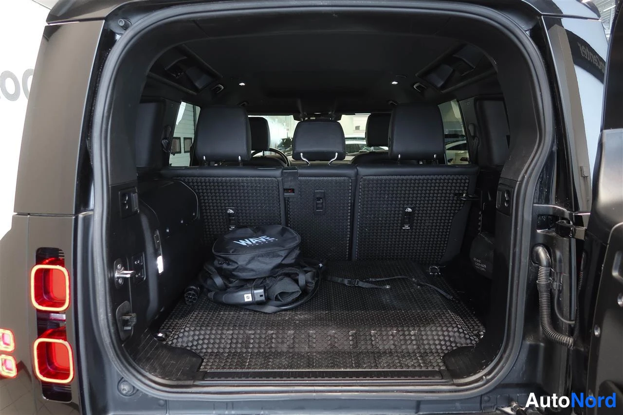 Takaa: Avattu takaistuoli ja tavaratila tummassa Land Rover Defender 110:ssä; lattiamatto ja musta laukku merellä.
