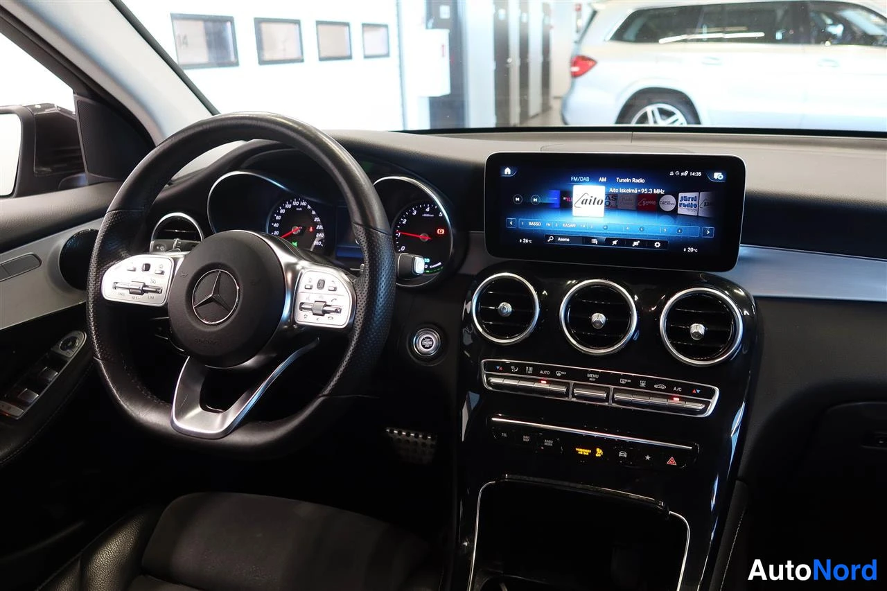 Muu: Mercedes-Benz GLC:n kojelauta: monitoimiohjauspyörä, analogiset mittarit, keskellä kolme pyöreää ilmastointisuutinta ja suuri kosketusnäyttö, jossa näkyy radion