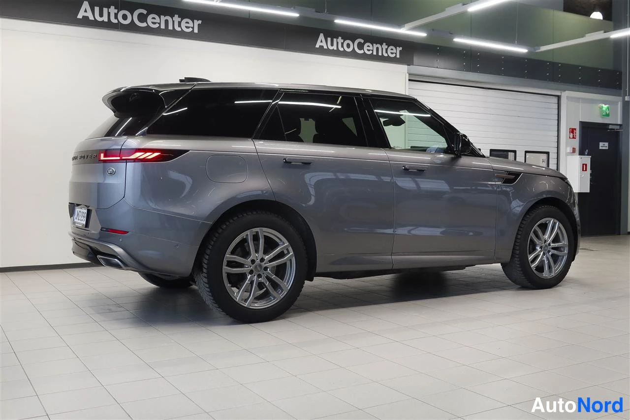 Takaviisto: Hopeanharmaa Land Rover Range Rover Sport takaa-kuvasuuntaisuudessa showroom-lattialla; takavalojen viiva, sivulinja ja metallivanteet näkyvät.