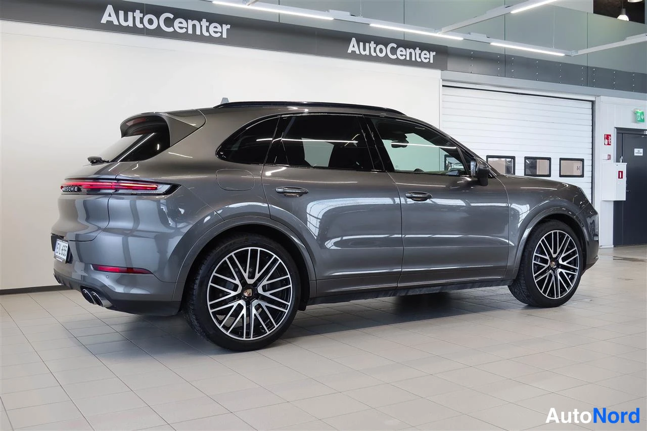 Takaviisto: Harmaa Porsche Cayenne -maastauto sivulta takaa kuvattuna myyjätilassa.