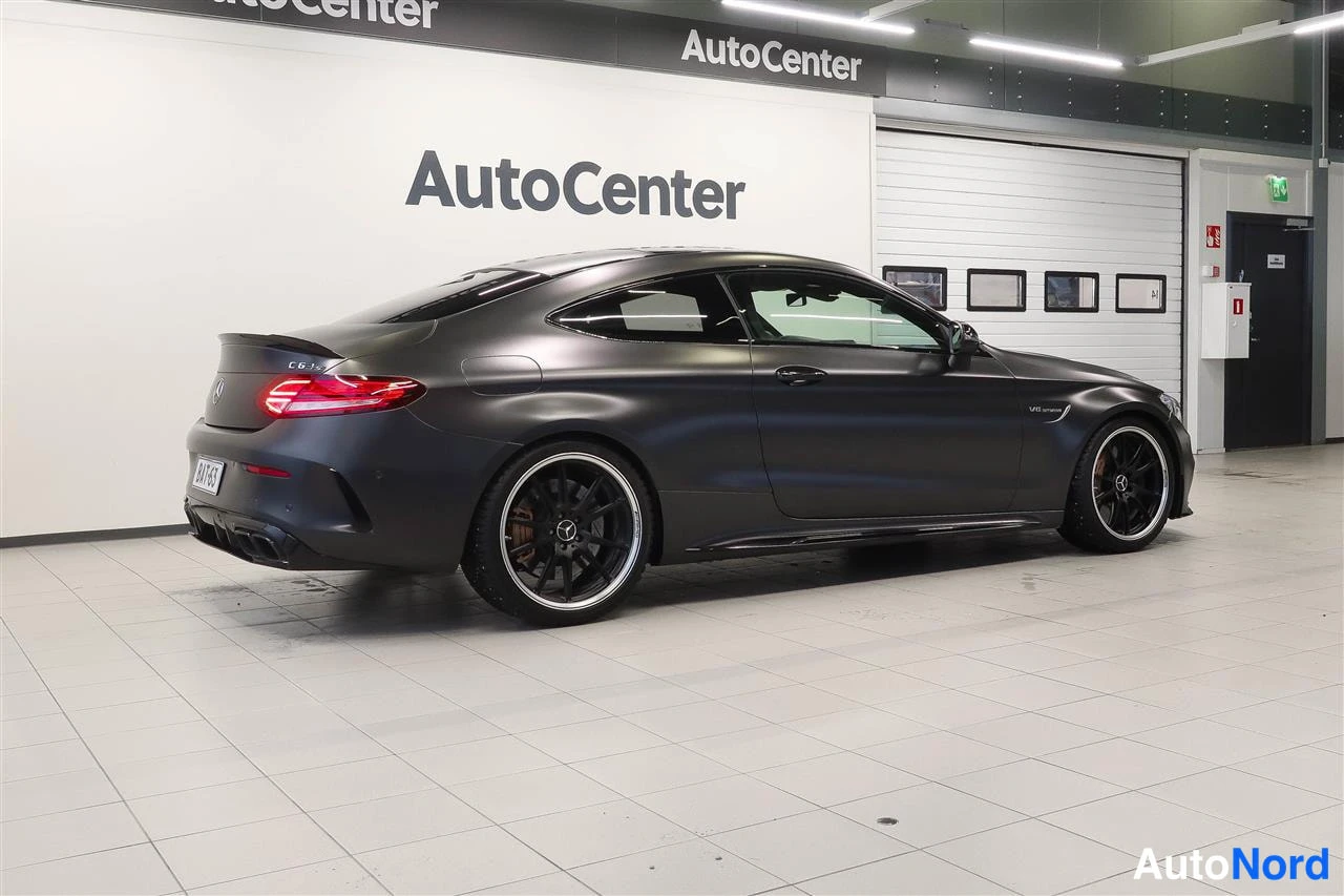 Takaviisto: Tummanharmaa Mercedes-Benz C 63 -coupe takaa vasemmalta nähtynä myyntihallissa.