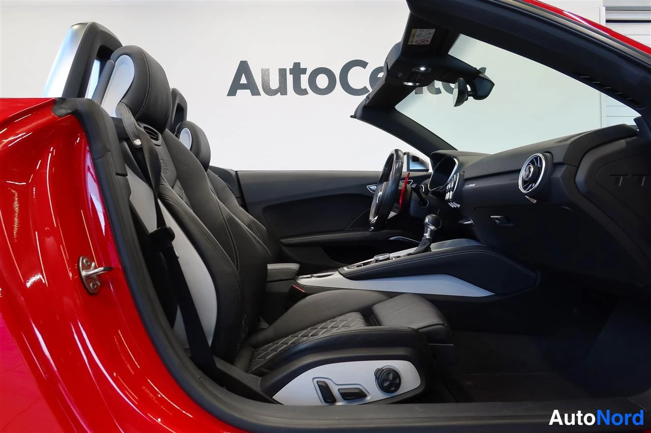 Muu: Punainen urheilutekstiiliauto / avoauto sisätilat: kaksi istuinta, ohjauspyörä, keskikonsoli, avattu katto, taustalla AutoCenter-tunnus.