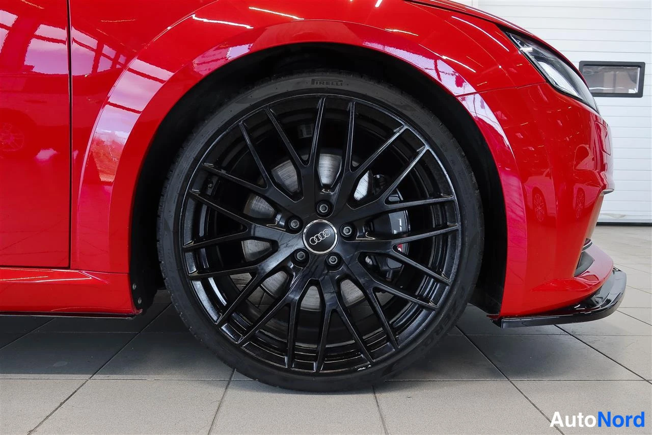 Etuviisto, nokka oikealle: Punaisen auton etupyörän lähikuva, musta monipuolainen kevytmetallivanne ja Pirelli-rengas, etusuoja ja kylki näkyvissä.