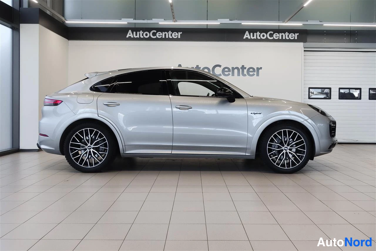 Etuviisto, nokka oikealle: Hopeinen Porsche Cayenne Coupé -tyylinen SUV sivulta etukulmasta oikeaan, näkyvissä kyljet ja osittain keula.