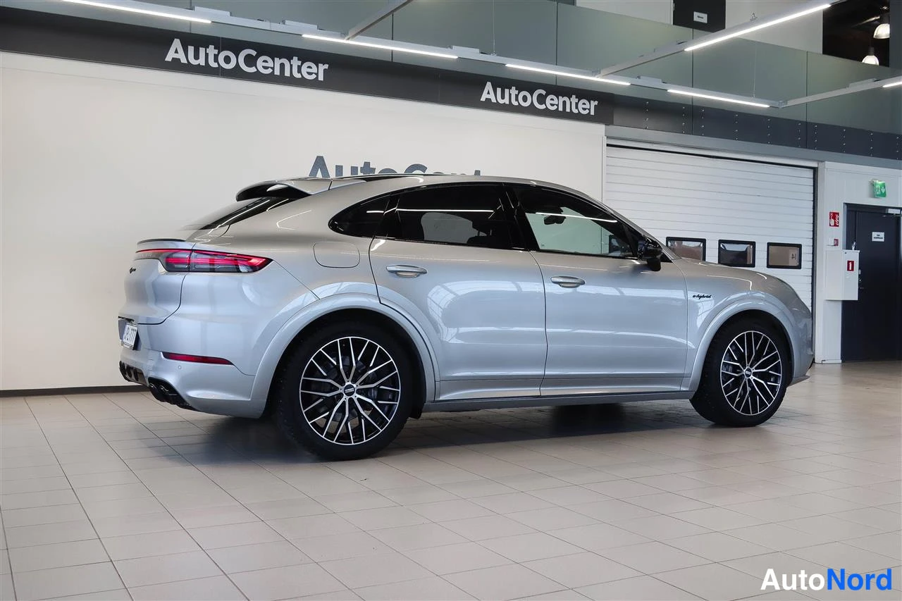 Takaviisto: Hopeanvärinen Porsche Cayenne Coupé takaviistokuvassa automyymälän lattialla.