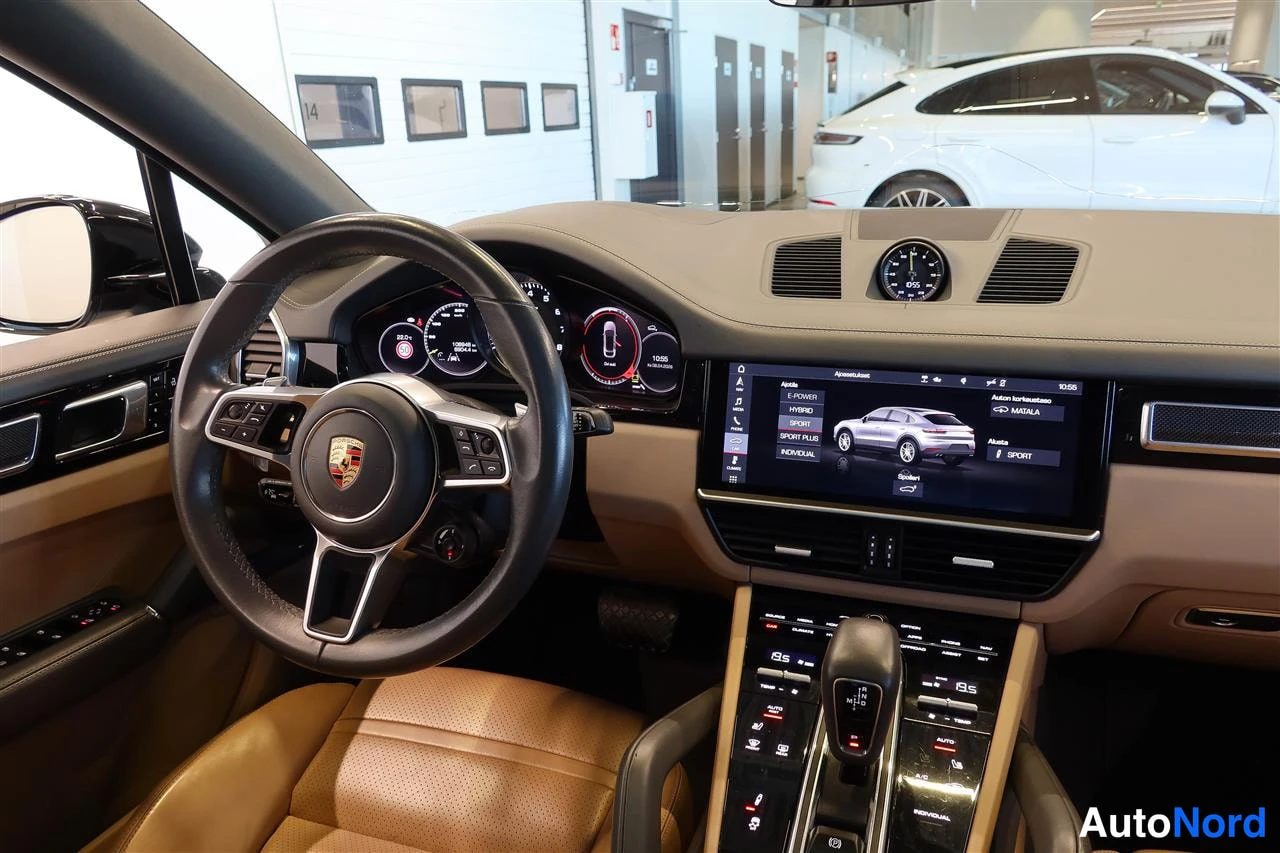 Muu: Porsche Cayennen kojelauta ratin ja kosketusnäytön kanssa; näytöllä ajotilavalikko E-HYBRID, HYBRID, SPORT, SPORT PLUS ja INDIVIDUAL.