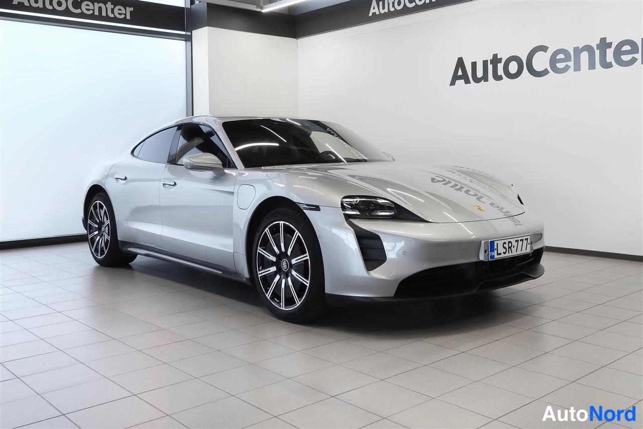 Etuviisto, nokka oikealle: Hopeanhohtoinen Porsche Taycan edessä vasemmasta kulmasta, rekisterikilpi, AutoCenter-hallissa.