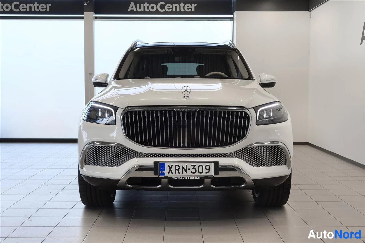 Edestä: Valkoisen Mercedes-Benz GLS Maybachin etunäkymä, pystysäleinen virtapiiri­rit, rekisterikilpi, LED-ajovalot päällä, AutoCenter-hallissa.