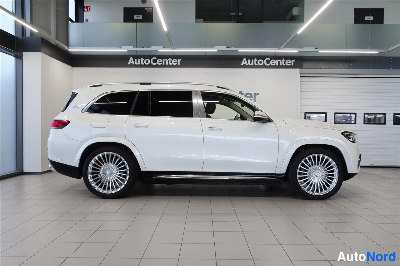 Takaviisto: Valkoisen Mercedes-Benz GLS Maybachin taka­viisto vasemmalta, kromiset sivulistat, moni­kiekkoiset vanteet, AutoCenter-hallissa.