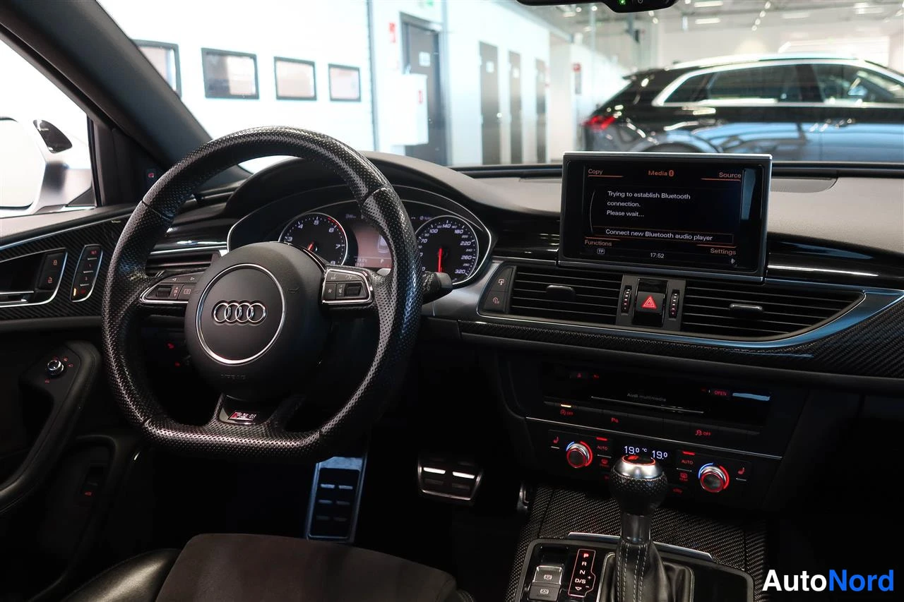 Sivulta: Kojelaudan näkuva Audi-ohjauspyörällä, analogisilla mittareilla ja taustapeilin näytöllä, jossa Bluetooth-yhdistysviesti.