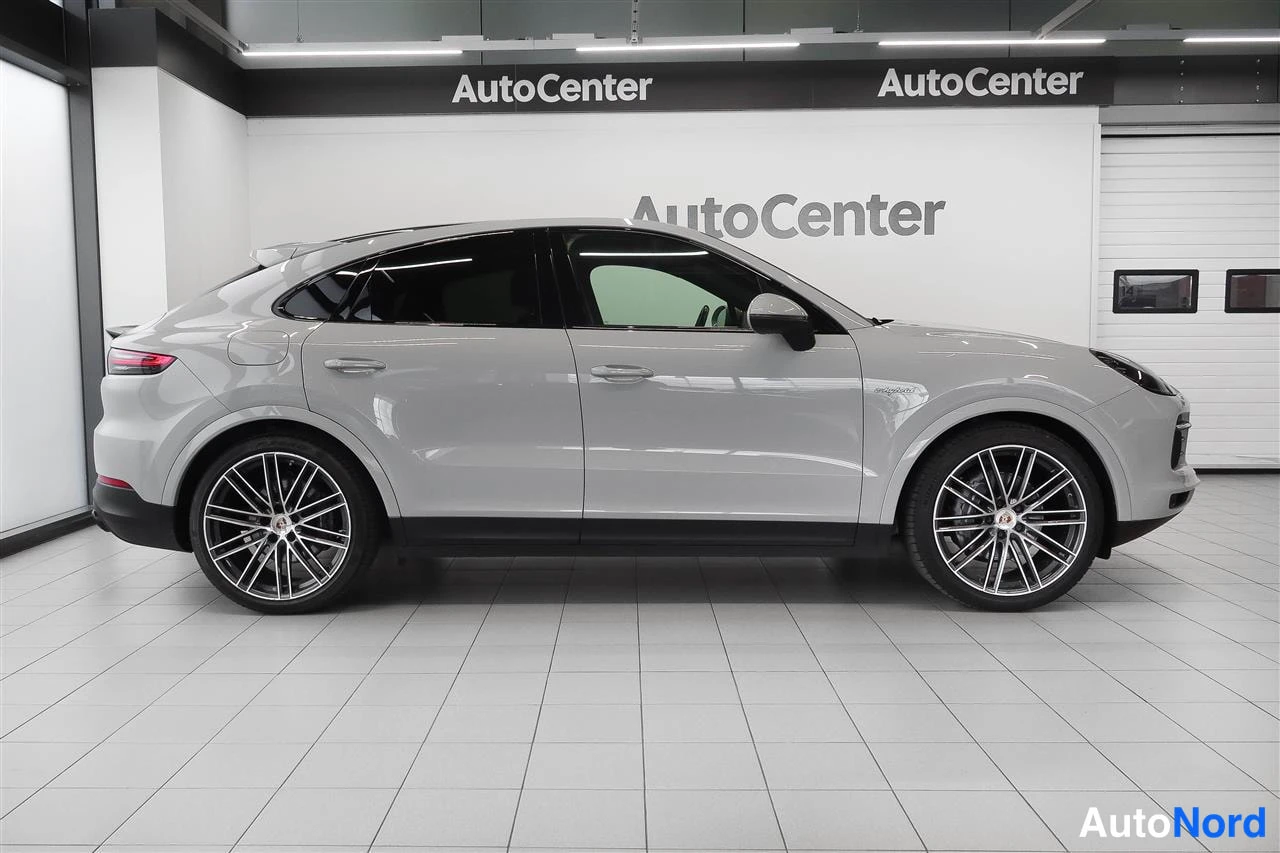 Takaviisto: Porsche Cayenne Coupén sivuprofiili, takavalojen ja ovien näkyessä, AutoCenter-hallissa.