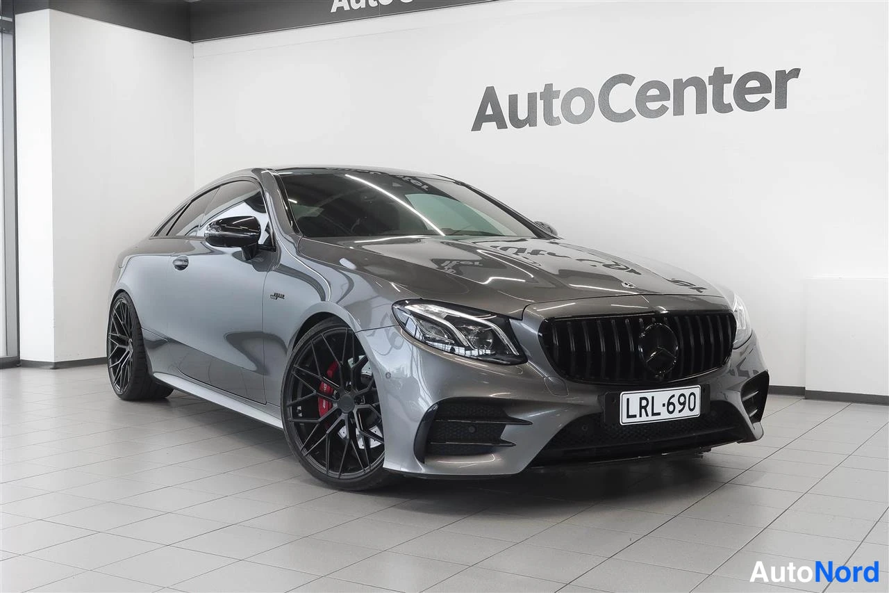 Etuviisto, nokka oikealle: Mercedes-Benz E 53 AMG -kupé etukulmasta, harmaa kori ja mustat vanteet AutoCenter-tilassa.