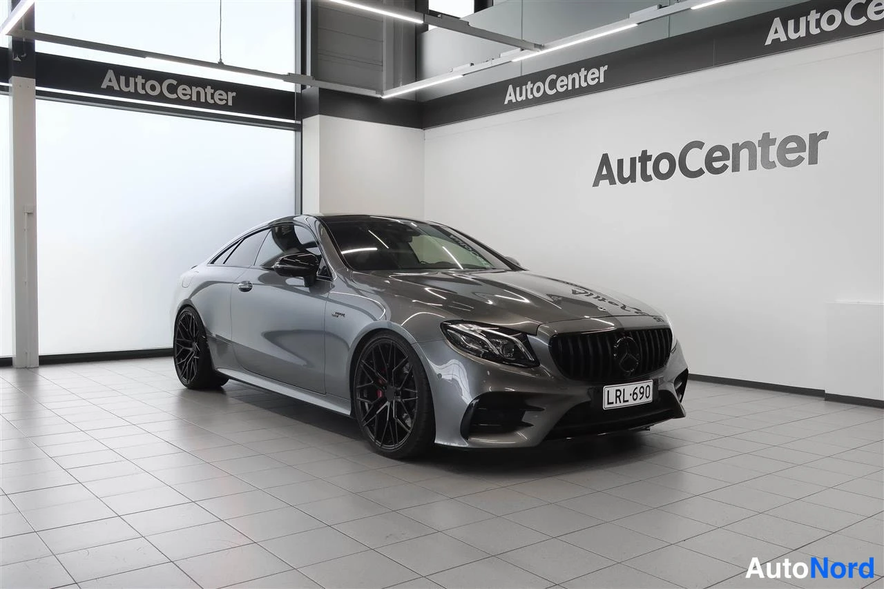Etuviisto, nokka oikealle: Mercedes-Benz E 53 AMG -kupé etukulmasta nähtynä, harmaa kori, AutoCenter-näyttelytilassa.