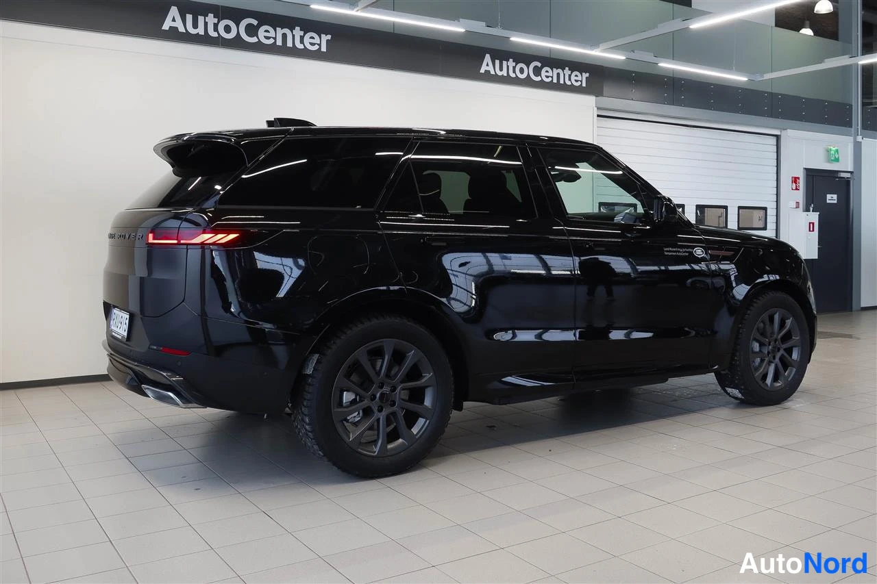 Takaviisto: Musta Range Rover Sport takaa sivulta kuvattuna myyntihallissa; rekisterikilpi ja takavalot näkyvissä.