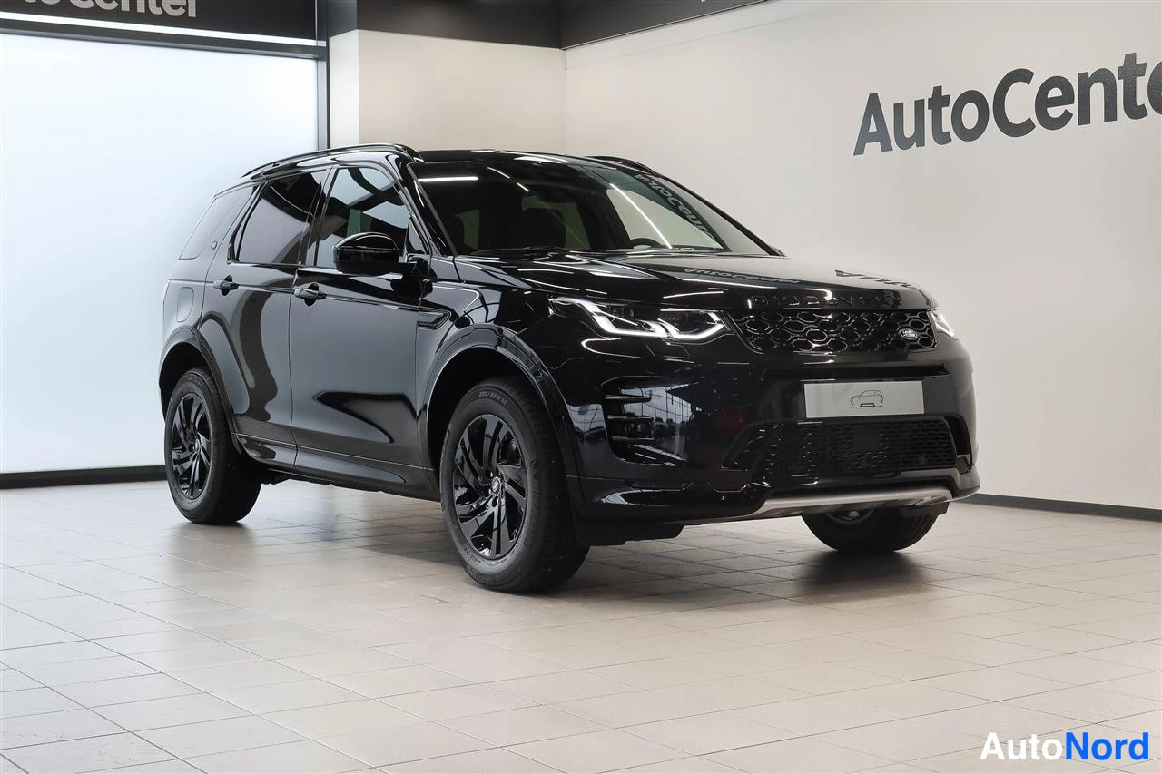Etuviisto, nokka oikealle: Musta Land Rover Discovery Sport etuviistosta oikealta autonäyttelytilassa