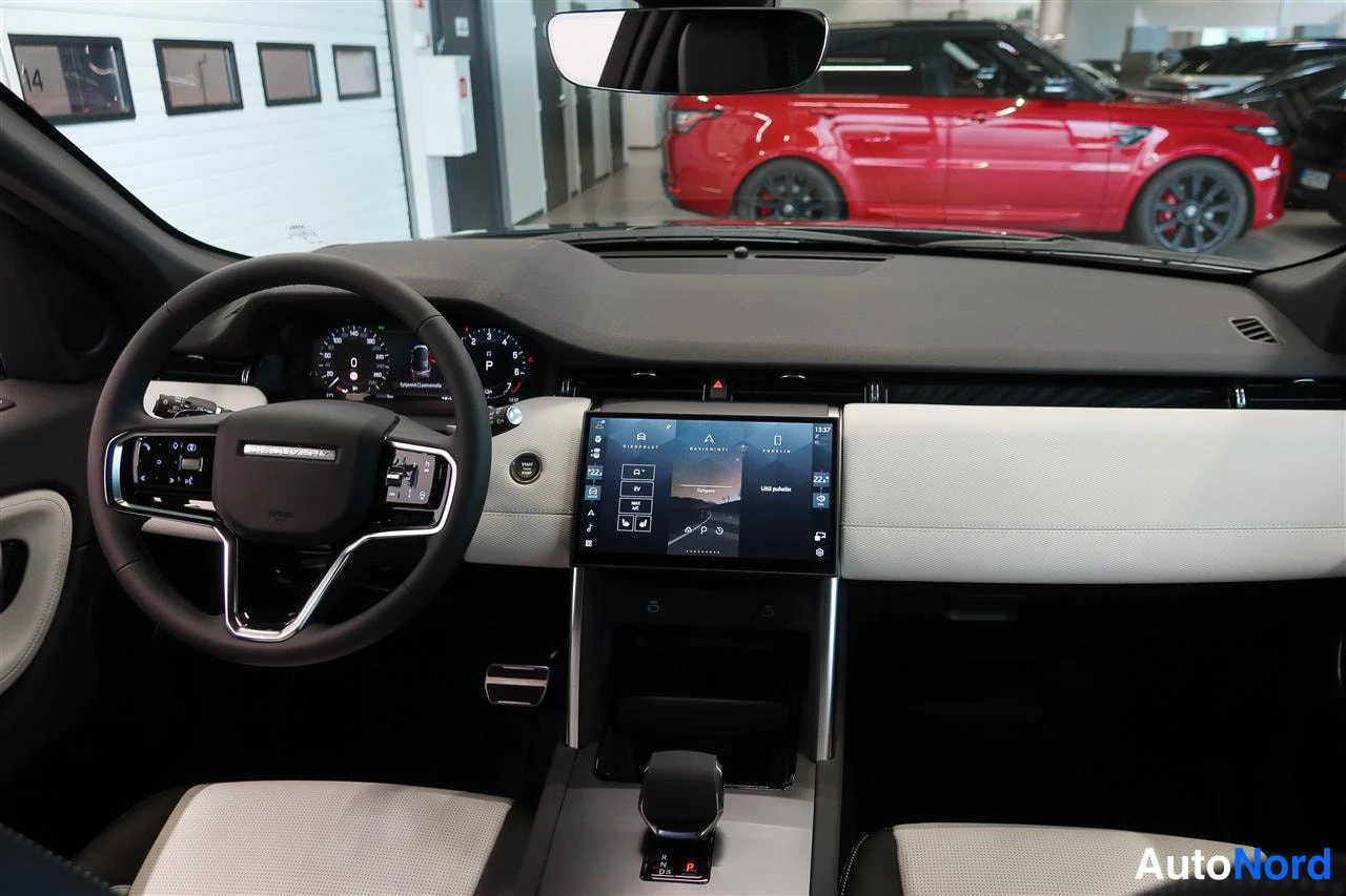 Edestä: Ohjaamon näkymä: Land Rover -ohjauspyörä, analogiset mittarit ja keskellä kosketusnäyttö, jossa näkyy valikko ja teksti USB galaxy. Takana punainen toinen auto