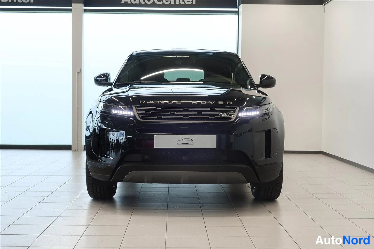 Edestä: Mustan Range Roverin suora etunäkymä, etusäleikkö ja ajovalot näkyvät, taustalla AutoCenter-kyltti.