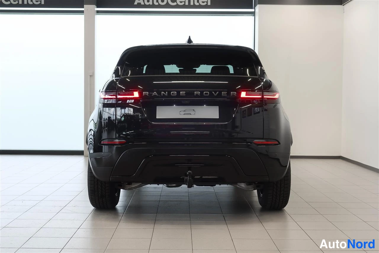 Takaa: Mustan Range Roverin takanäkö myyntihallissa; syttyneet takavalot, 'RANGE ROVER' -teksti ja trukkihistorja näkyvät.