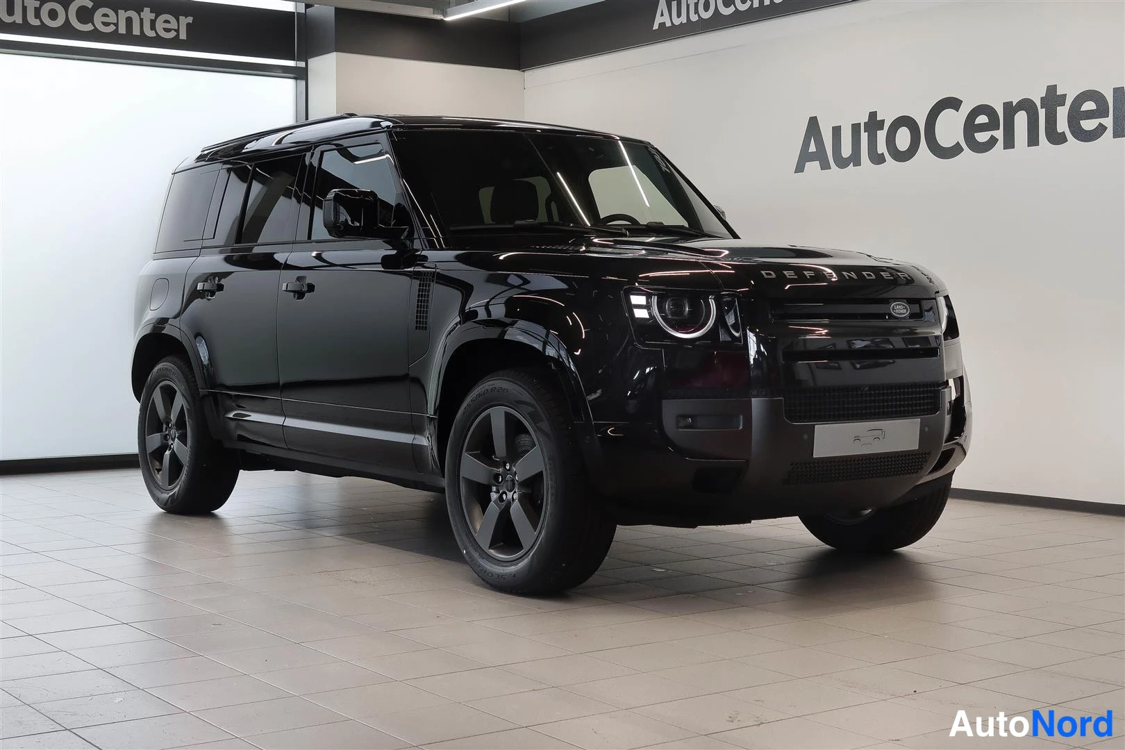 Etuviisto, nokka oikealle: Mustan Land Rover Defenderin etukulmakuva auton hallissa, keula oikealla.