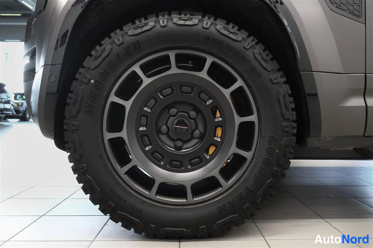 Muu: Renkaan lähikuva, Goodyear Wrangler DuraTrac RT -rengas mustalla vanteella ja keltainen jarrusatula.
