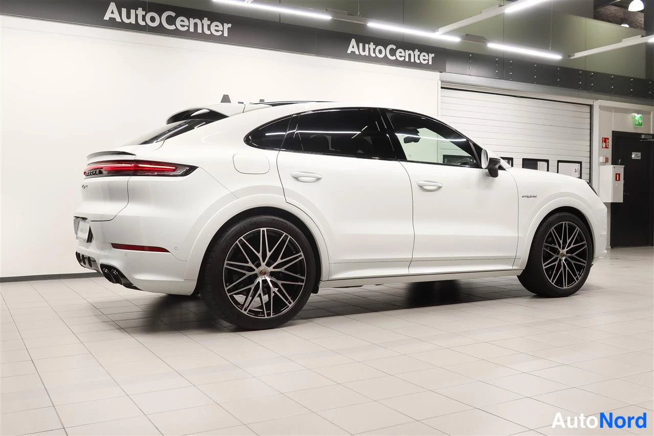 Takaviisto: Porsche Cayenne Coupé valkoisena takakulmasta sisätiloissa, näkyvissä takavalo, korimallin takaosa ja mustat vanteet.