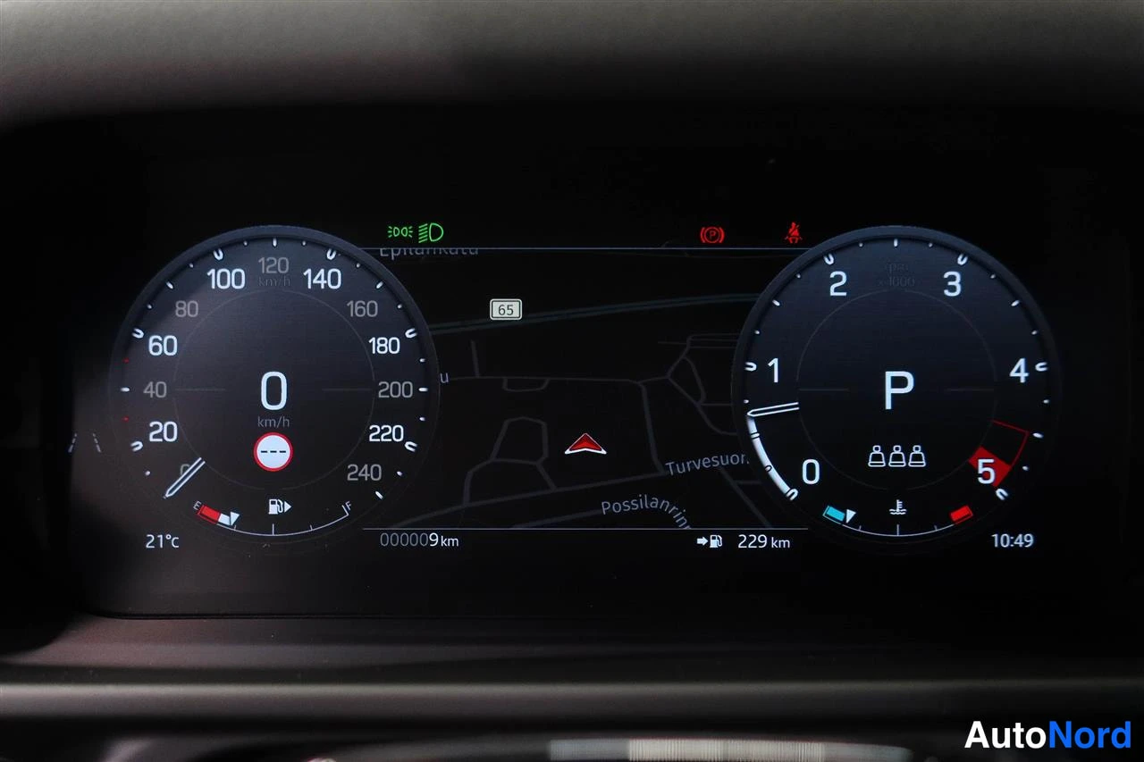 Yksityiskohta: Digitaalinen mittaristo: nopeusmittari 0 km/h, vaihde P, matkamittari 9 km, ulkolämpötila 21 °C ja karttanäkymä näytöllä.