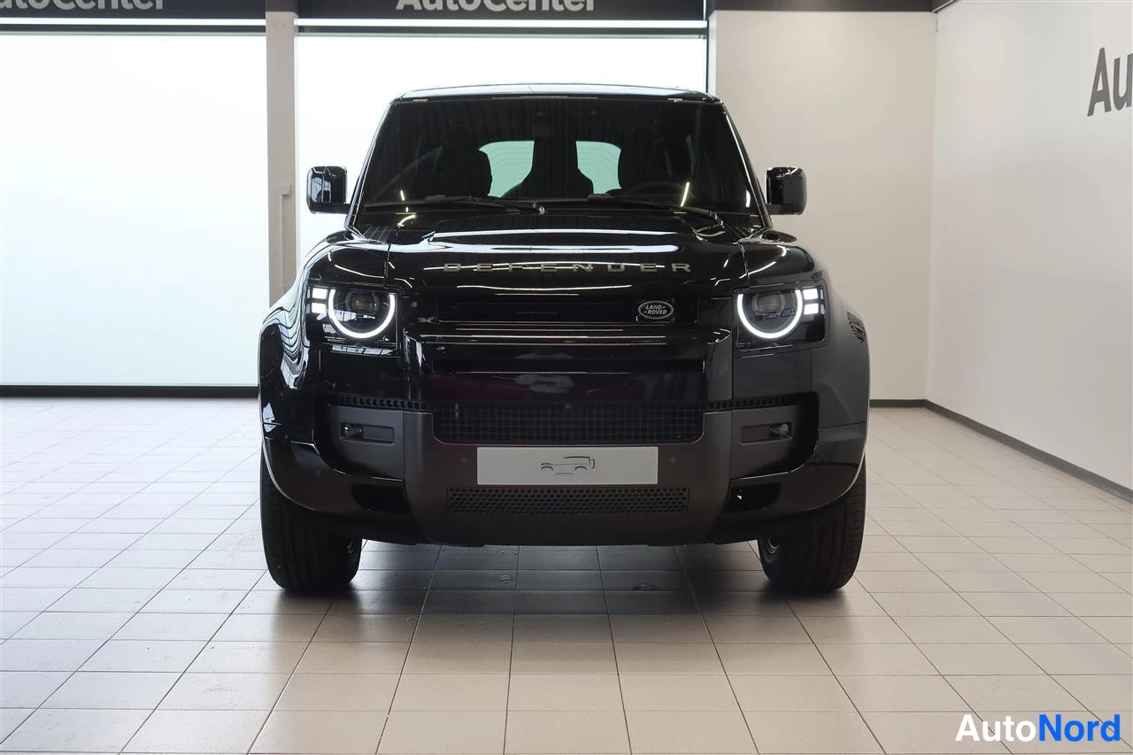 Edestä: Mustan Land Rover Defenderin etupään suora kuvaAutoCenter-tilassa, DEFENDER-kyltti konepellillä.