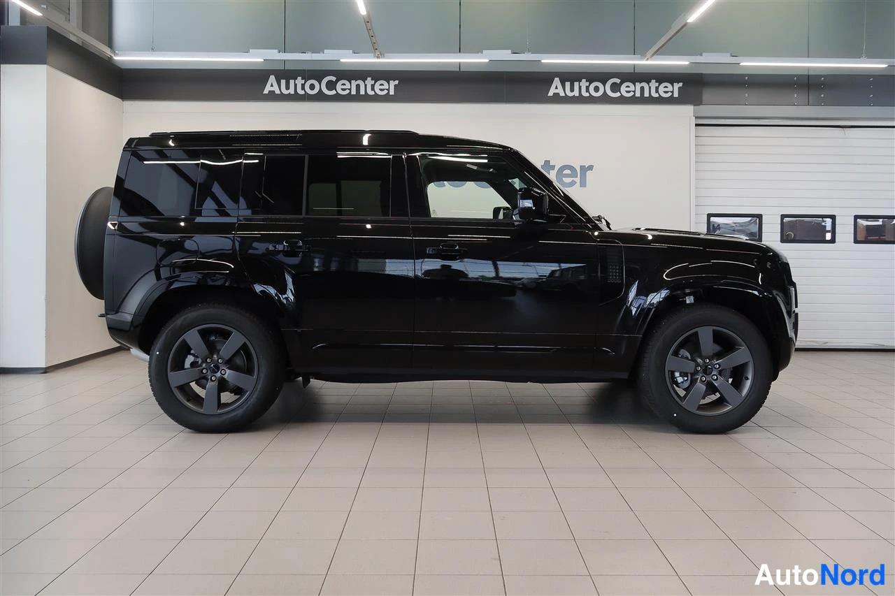 Sivulta: Mustan Land Rover Defenderin sivuprofiili vasemmaltaAutoCenter-tilassa, varapyörä takana.