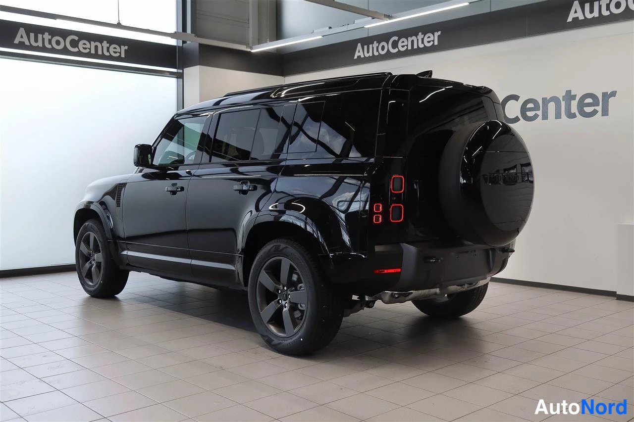 Takaviisto: Mustan Land Rover Defenderin takaosa ja sivu näkyvät kuvassa, varapyörä takaluukussa ja punaiset takavalot.
