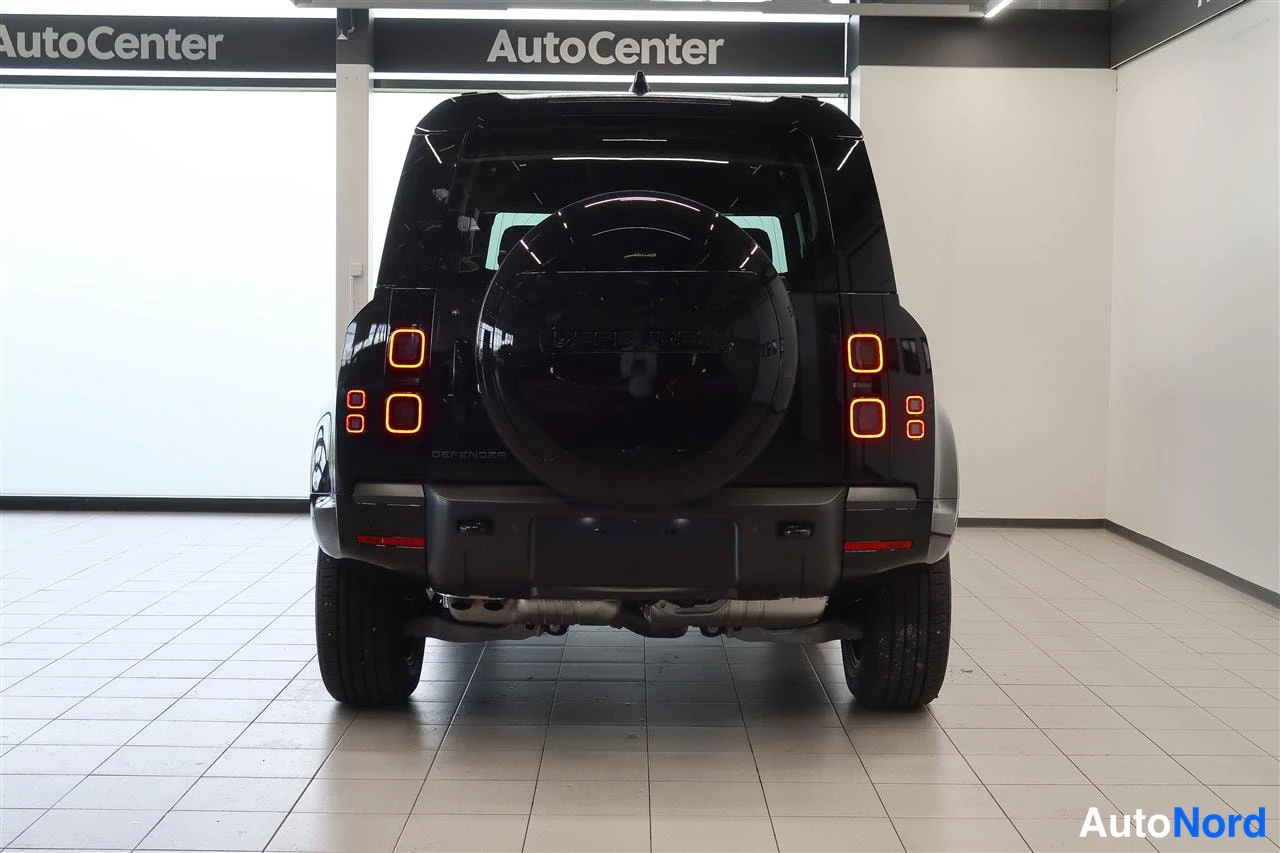 Takaa: Land Rover Defenderin takaosa suoraan takaa kuvattuna, varapyörä kannella ja oranssit takavalot syttyneinä.