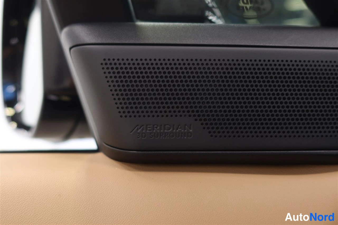 Yksityiskohta: Tummansininen teksti 'MERIDIAN 3D SURROUND' kaiuttimen ritilässä, beigea nahkaa ympärillä.